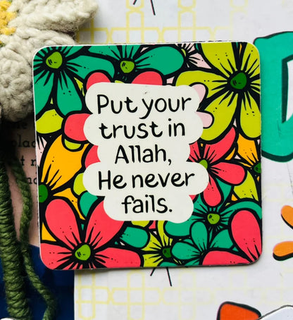 A square decorative card or coaster with rounded corners featuring a colorful retro floral pattern and the printed phrase, 'Put your trust in Allah, He never fails.' in black text on a white cloud-shaped label.
